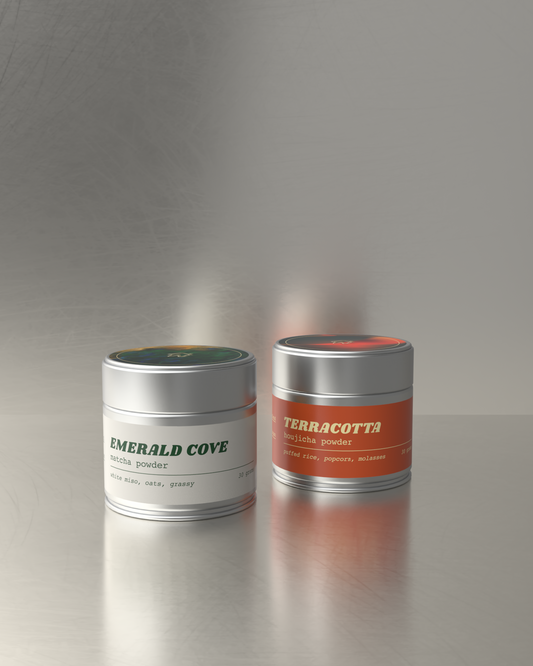 Teawerx two metal containers labeled 'Emerald Cove' and 'Terracotta' on a reflective surface with a gray background.
