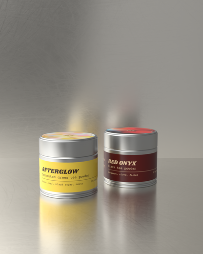 Teawerx Discovery Gift Set featuring Afterglow fermented tea powder and Red Onyx black tea powder in premium metal tins on a reflective gray surface
background.